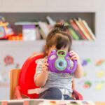girl holding purple and green camera toy